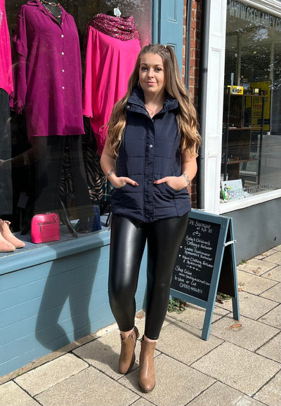 Woman wearing a navy gilet and leather trousers outside the boutique